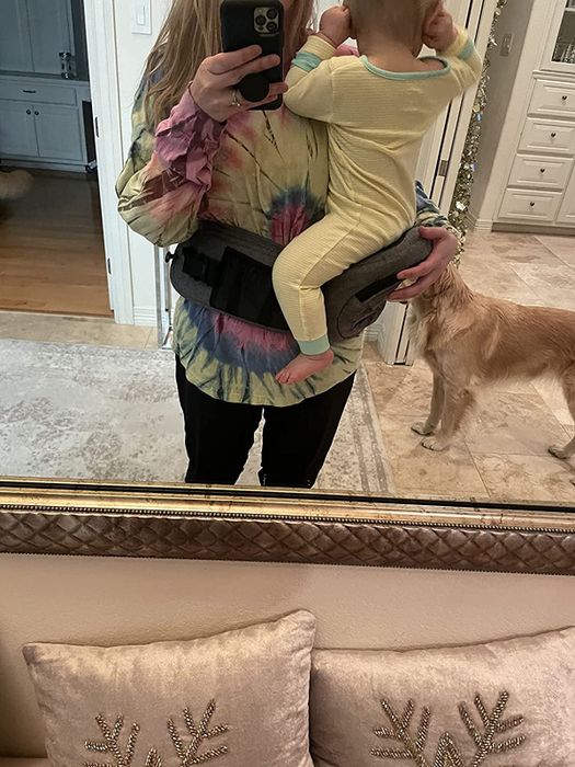 A reviewer demonstrating how the carrier wraps around their waist, making it easy to hold a baby.