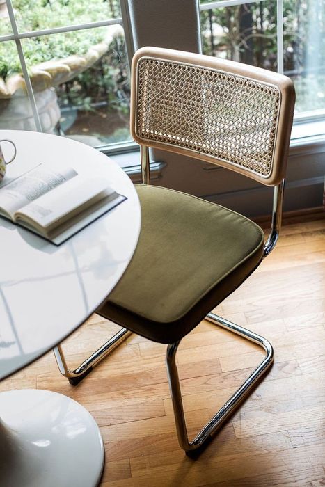 A modern chair featuring a woven backrest beside a round table with an open book, set in an indoor space