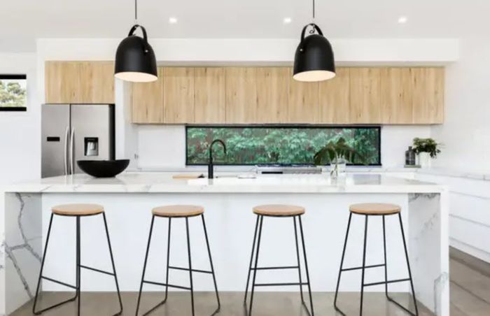 A sleek modern kitchen design featuring an island, stools, and pendant lighting, with a view of lush greenery through a horizontal window.