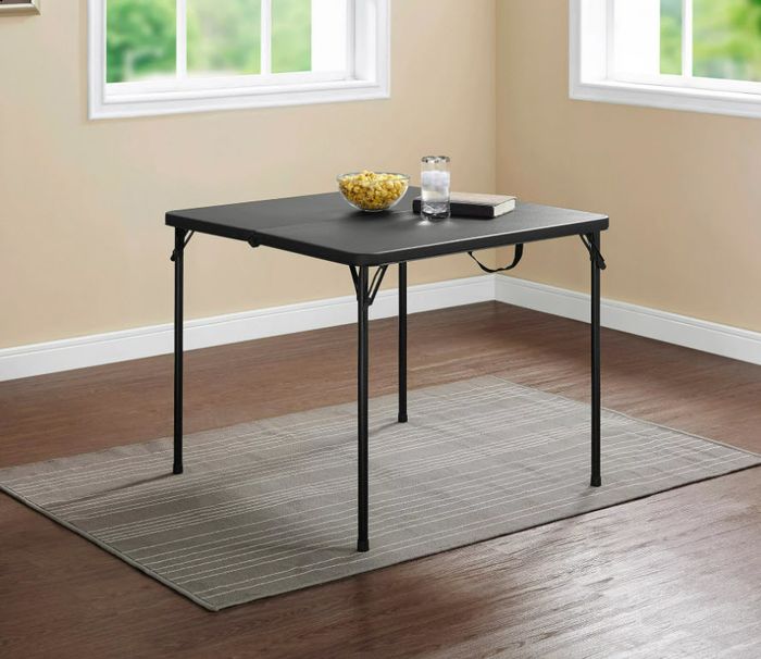 A simple folding table topped with a bowl of popcorn and a glass of water, placed on a rug by a window in a cozy room.