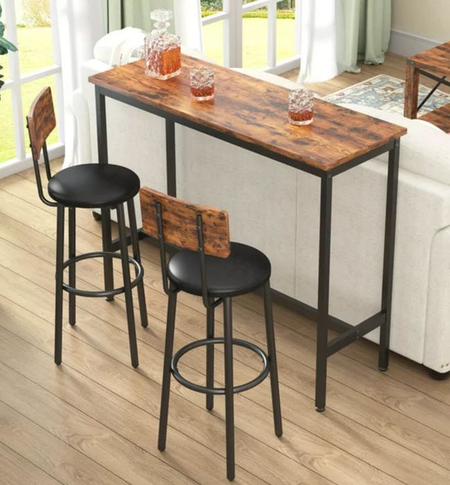A wooden bar-height table with two matching stools set against a bright, airy room near a window.
