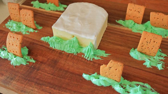 Green-dyed cream cheese with crackers on a cutting board.