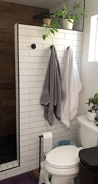 A bathroom featuring a white tiled shower wall, a toilet, neatly hung towels, and potted plants.