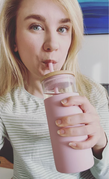 Editor holding a glass tumbler with a pink silicone lining and matching straw
