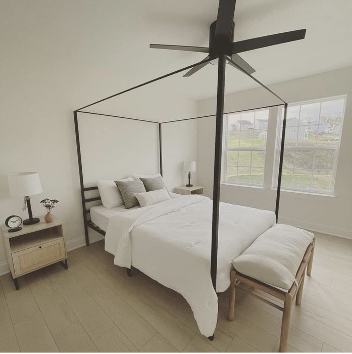 A minimalist bedroom featuring a four-poster bed, a nightstand with a lamp, and a bench at the foot of the bed
