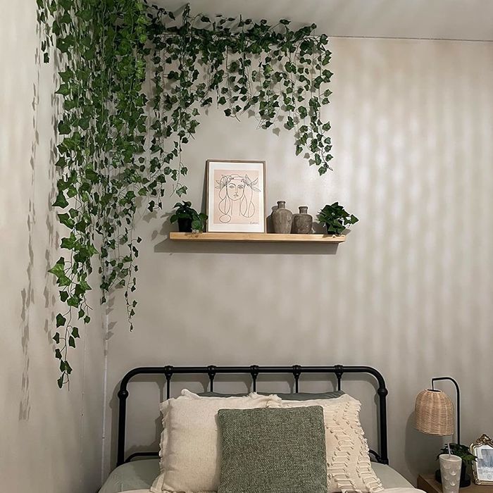 A bed adorned with pillows beneath a shelf showcasing plants and decorative items, positioned above a sleek metal headboard
