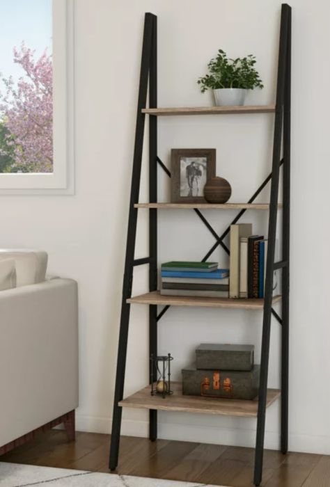 A five-tier ladder-style bookshelf, neatly arranged with books and decorative pieces, positioned next to a cozy couch.