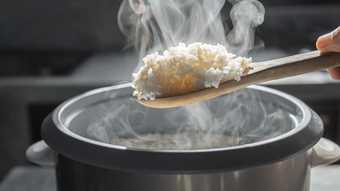 A wooden spoon serving rice from the rice cooker.