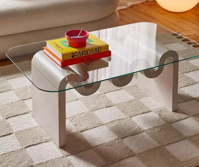 A sleek glass coffee table with curved edges, topped with a stack of books