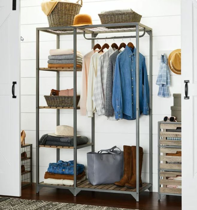 A metal storage unit with shelves, neatly organizing clothes, shoes, baskets, and a gray bag. No people are present in the image.
