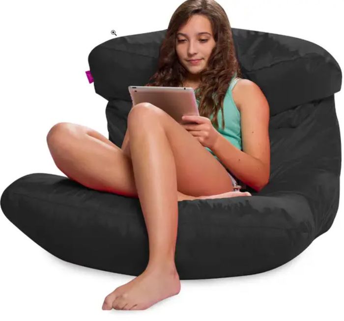 A person relaxing on a black beanbag chair while using a tablet.