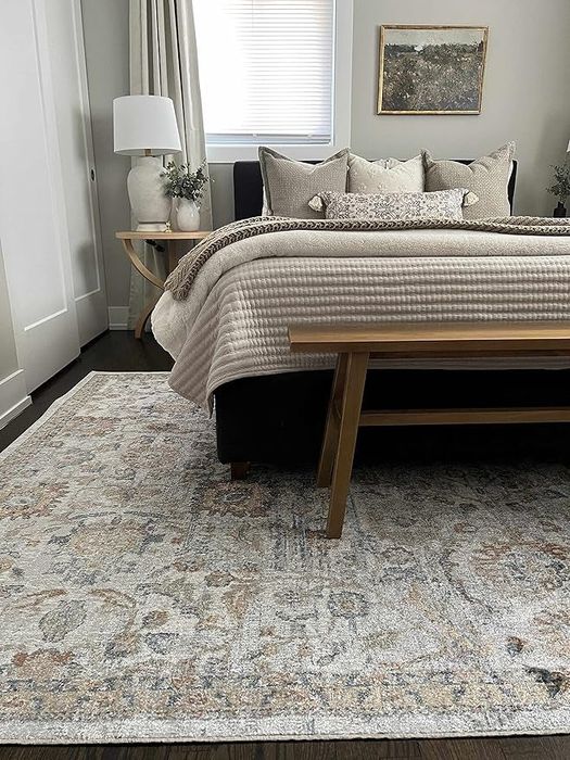 A stylish bedroom featuring a patterned area rug, a bed with neutral-toned bedding, and a lamp on a nightstand