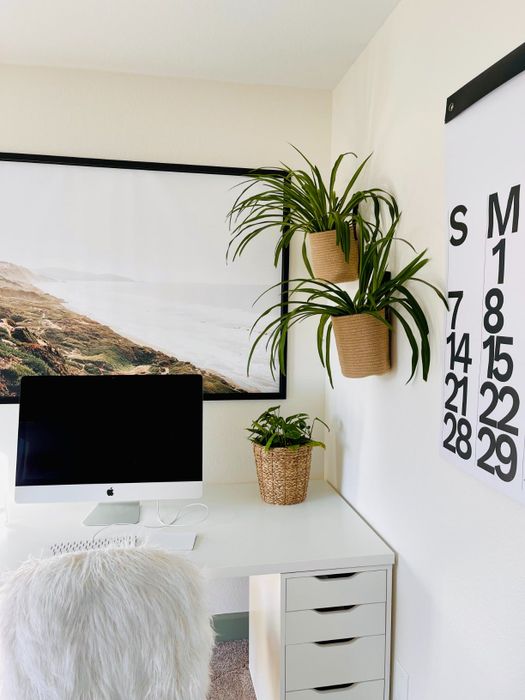 A cozy home office setup featuring a desktop computer, a wall-mounted calendar, and two stylish hanging planters.