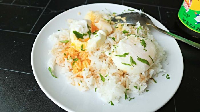 Two poached eggs served on a bed of rice, topped with soy sauce and fresh herbs.