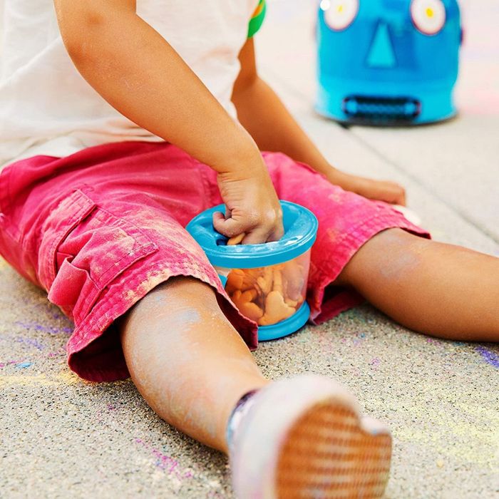 A child's hand reaching into the blue snack cup to pull out a cracker