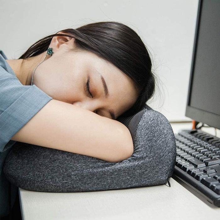 A person resting their head on the pillow while sleeping at their desk