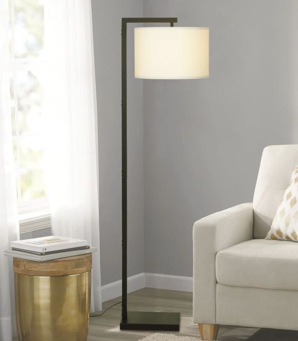 A floor lamp featuring a white shade, positioned next to a beige armchair in a stylish living room setting.