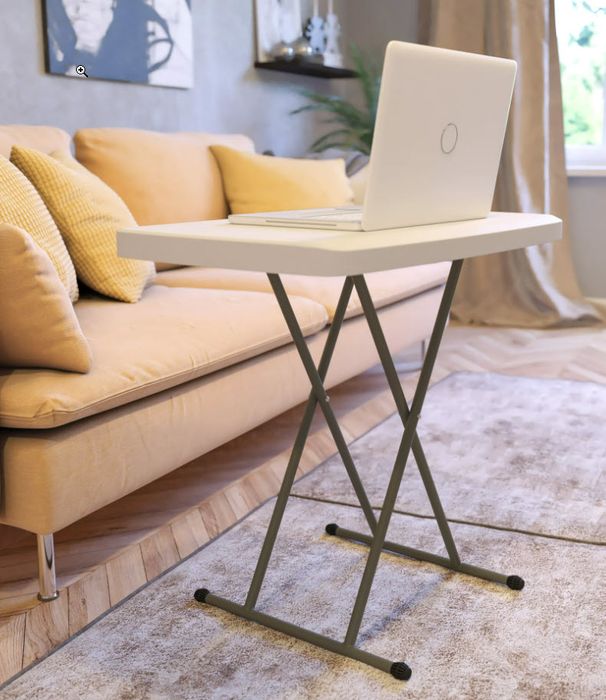 A laptop placed on a small, elevated desk in a cozy room, complemented by a couch and cushions for a comfortable working environment.