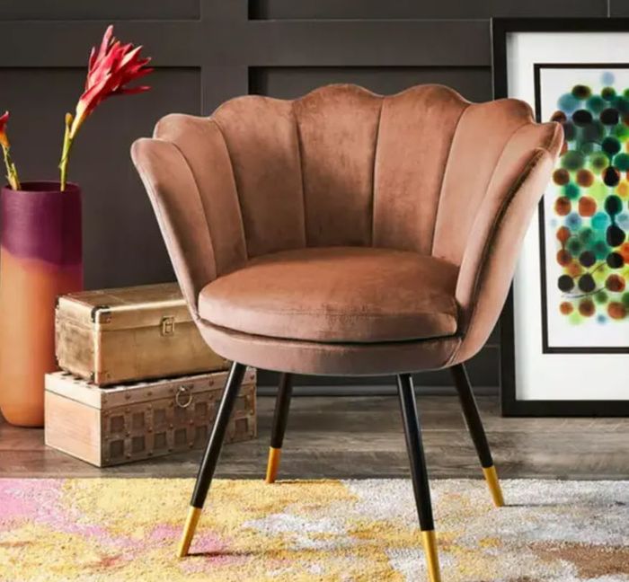 A luxurious clamshell-style velvet chair with sleek metal legs, placed beside a vintage suitcase and set against a bold modern art piece.