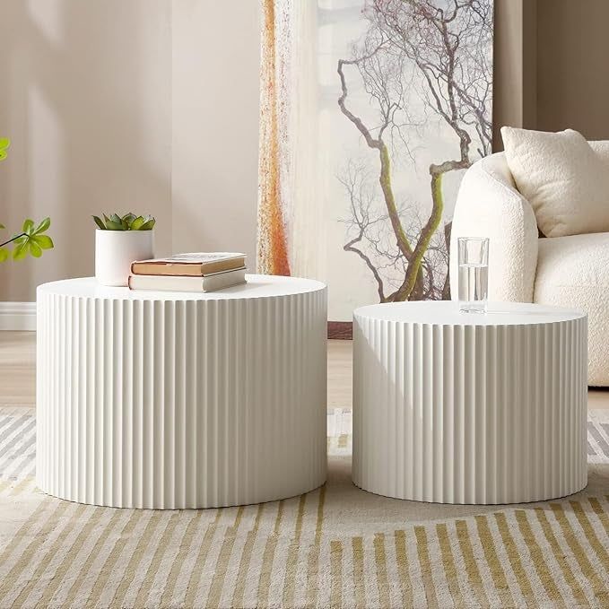 Two white ribbed cylindrical side tables, one holding books and a plant, the other with a glass of water, placed in a stylish living room