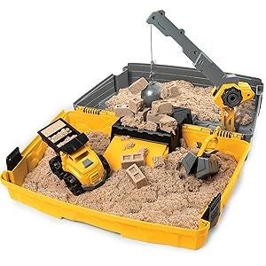 A toy construction site set featuring miniature vehicles, cranes, and bricks in a sand-filled play area