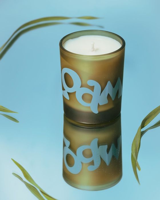 A candle in shades of blue and green rests on a reflective surface
