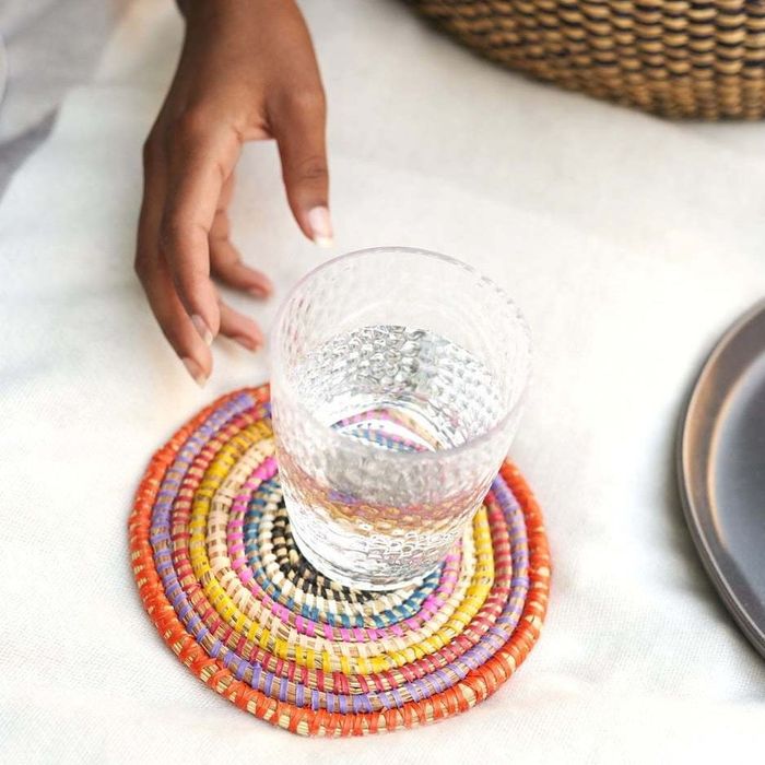 A hand placing a glass onto a vibrant beaded coaster on a tablecloth beside dinnerware