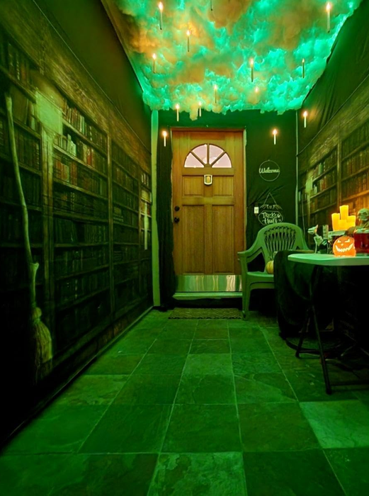 Hallway adorned with floating candles, a cloud-patterned ceiling, and wallpaper resembling bookshelves. A table with Halloween-themed decor and a pumpkin is placed near the door
