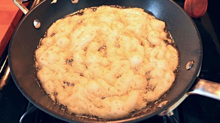 Batter for funnel cake sizzling in a frying pan.