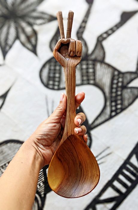 A person holds a large wooden spoon featuring an intricately carved handle