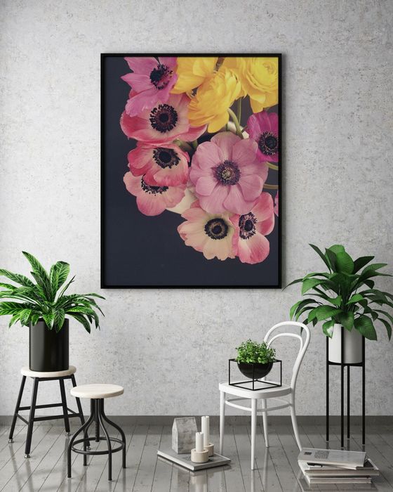 A large, framed floral piece hanging above a modern indoor plant arrangement, complete with a variety of stands and decorative pots.