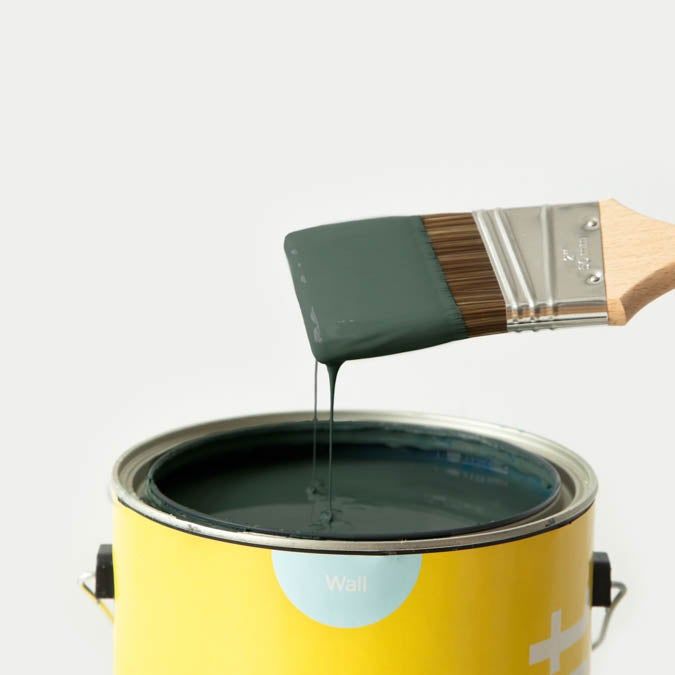 A green paintbrush dripping paint into a yellow paint can.
