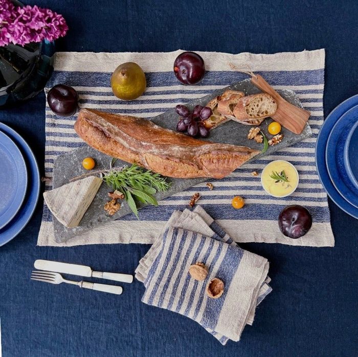 A beautifully arranged flat lay featuring a rustic loaf of bread, accompanied by cheese, fruits, nuts, and cutlery, all placed on a striped cloth.