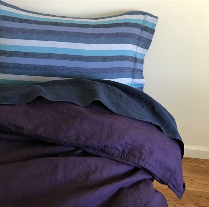 A bed adorned with purple and blue striped linen sheets