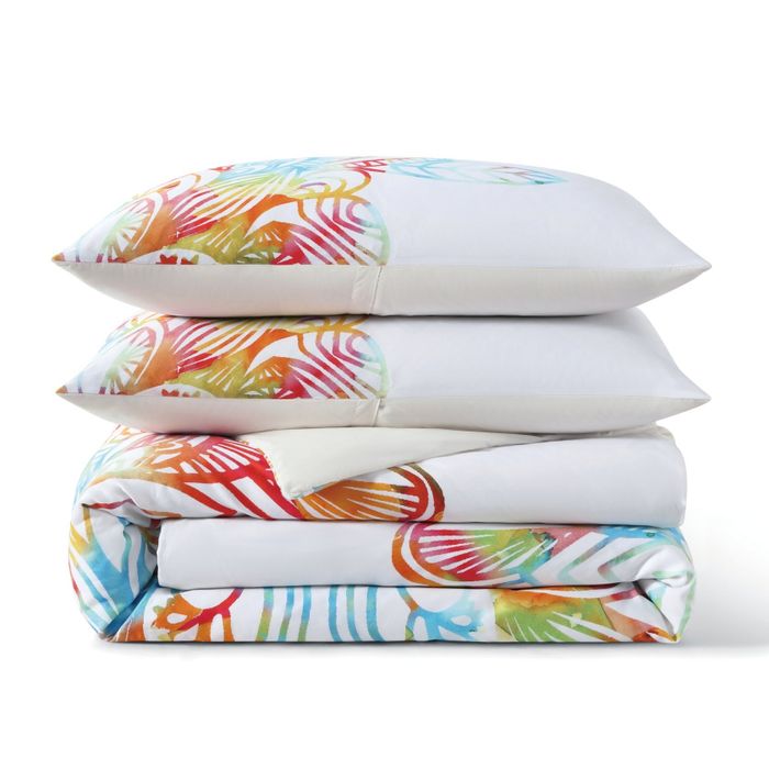 Stacked bed linens with bold tropical patterns, featuring a neatly folded duvet cover and three pillows
