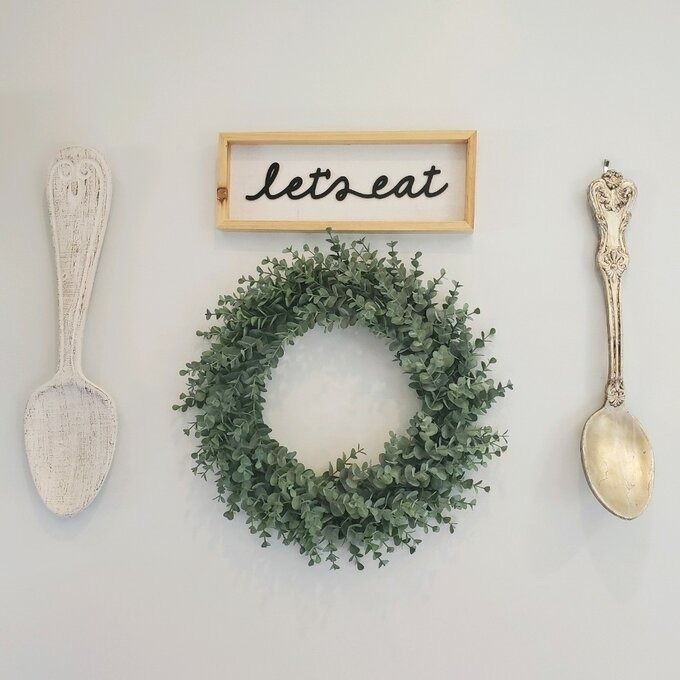 The wreath is hung beneath a sign that reads 'let's eat,' accompanied by two spoon decorations on either side
