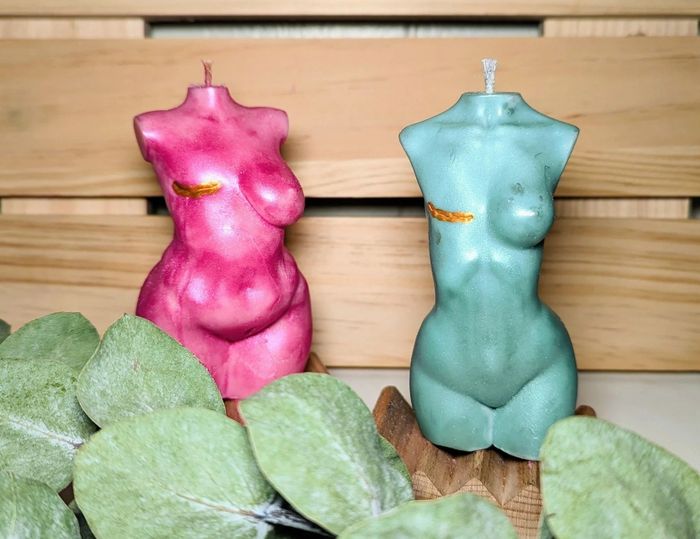 Two human-shaped candles featuring mastectomy scars on the chest are displayed
