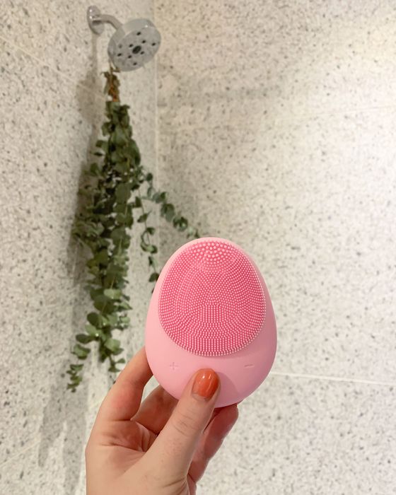 I'm holding up a palm-sized cleansing brush in my hand. It has a flattened egg shape, with soft silicone bristles on both sides.