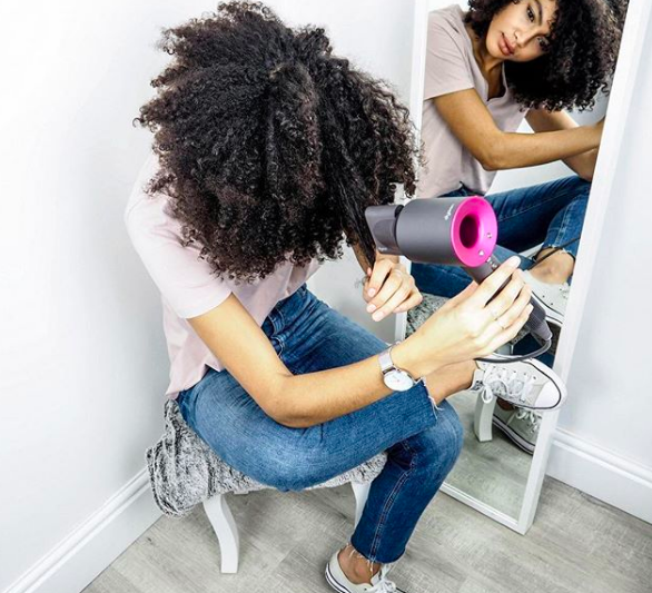 A person with curly hair blow-drying the ends of their hair.