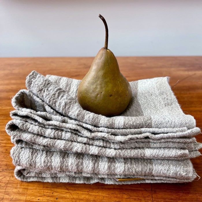 A crisp, fresh pear sitting elegantly atop a stack of neatly folded linen tea towels.