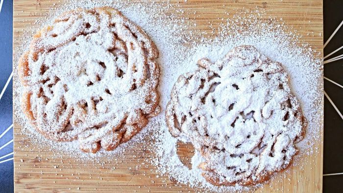 A pair of funnel cakes rests on a wooden cutting board.