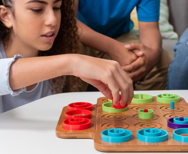 A player interacts with a board game, strategically placing a red piece on the board as two onlookers watch with keen interest