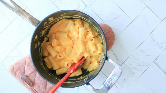 A pot of macaroni topped with a creamy yellow sauce, resting on a countertop.