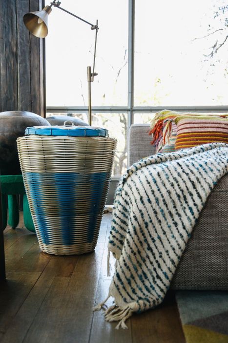 A wicker laundry basket placed beside a couch adorned with a striped blanket, creating a warm, inviting atmosphere in the room.