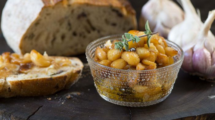 Roasted garlic placed in a bowl next to a fresh loaf of bread, ready for spreading.