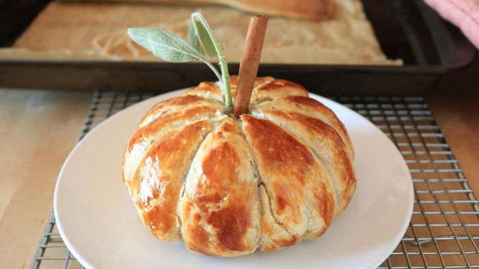 A pumpkin-shaped baked brie sits elegantly on a platter, ready to be enjoyed.