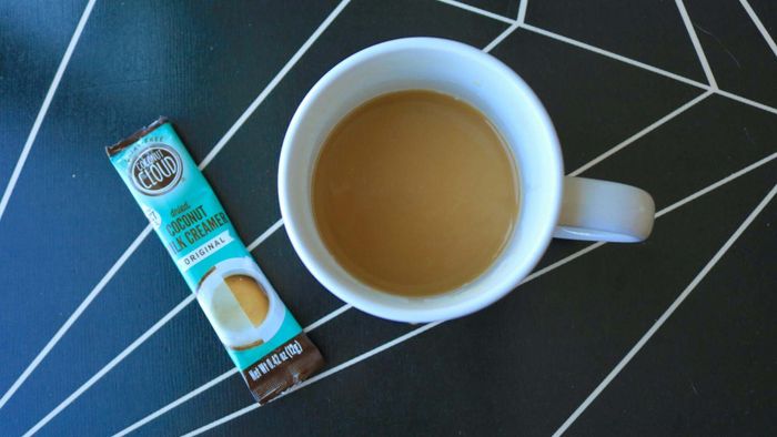 A cup of coffee with a Coconut Cloud sachet lying beside it, still unopened.