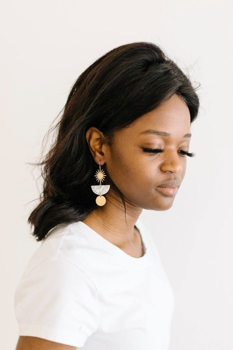 A model showcasing the drop earrings featuring a brass starburst design, a pink acetate semi-circle, and a brass circle
