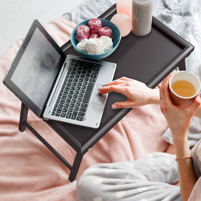 A black tray with dessert, tea, and a laptop resting on it.