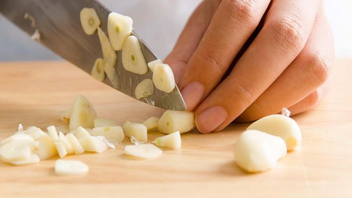 Slicing garlic cloves on a chopping board.